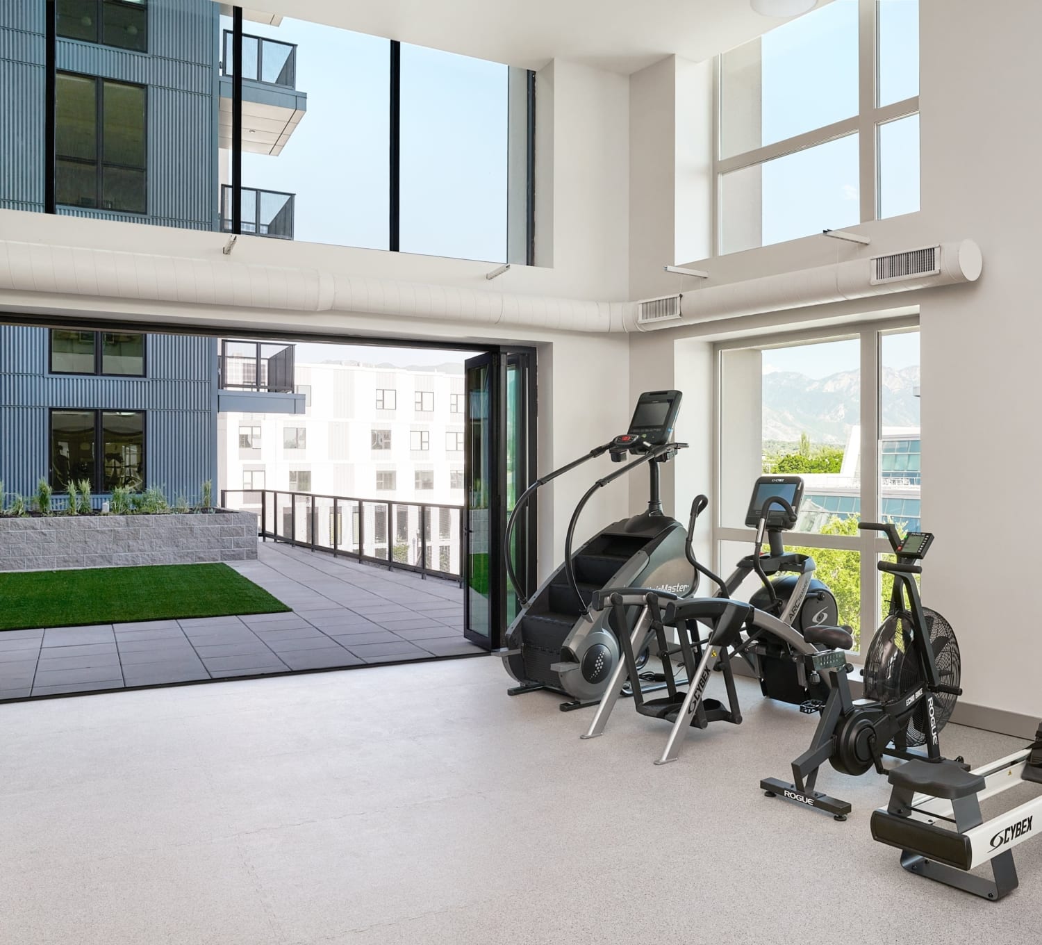 Fitness center with large windows and cardio equipment at Avia apartment community in Salt Lake City