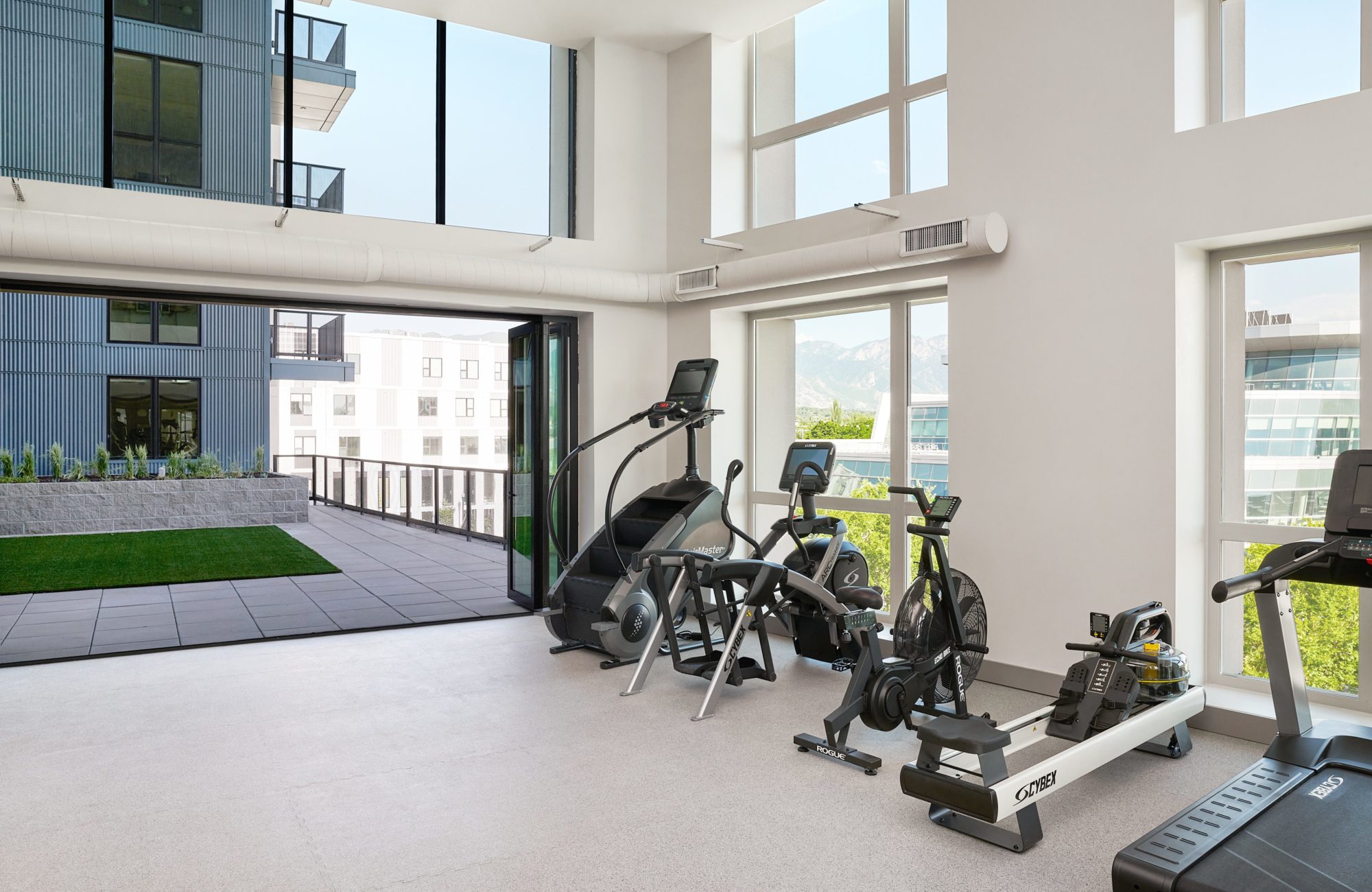 Fitness center with large windows and cardio equipment at Avia apartment community in Salt Lake City